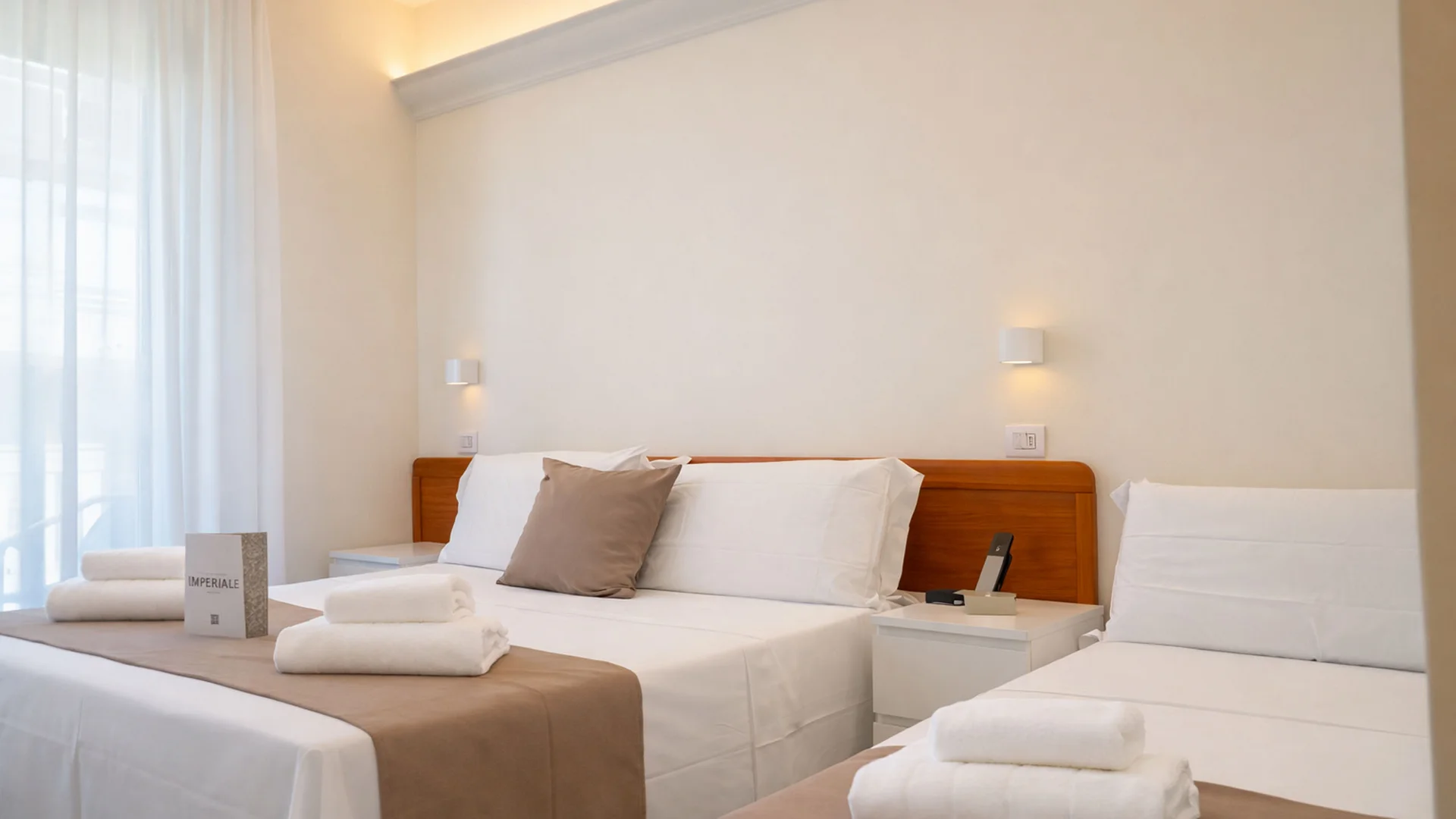 Hotel Regal: comfort ed eleganza a Rimini Camera d'albergo con letto matrimoniale, letto singolo, asciugamani bianchi e arredi chiari.